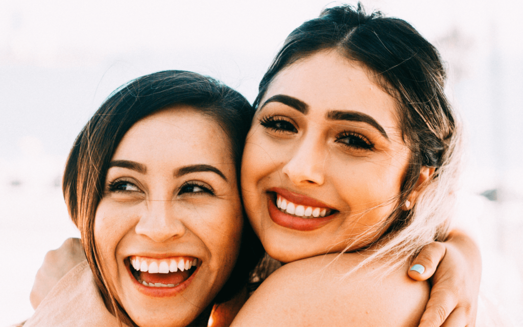 Two women hugging and smiling on California beach. 